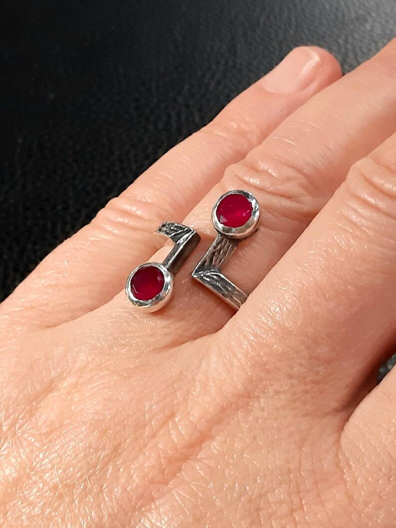 Op de afbeelding: Een zilveren ring met twee rode edelstenen in de band. De ring is ontworpen in de vorm van een noot.