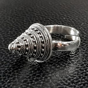 May include: A silver ring with a cone-shaped design. The cone is decorated with a series of concentric circles and small dots.