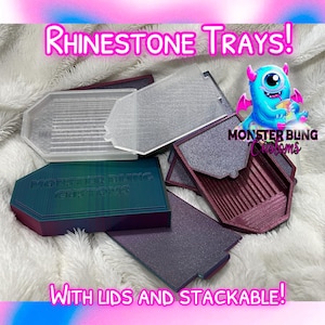 May include: Stackable rhinestone trays with lids. The trays are made of a clear plastic material and have a grid pattern on the bottom. The trays are labelled "Monster Bling Customs".