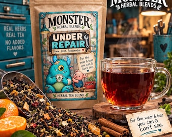 May include: A brown paper pouch of Monster Herbal Blends Under Repair tea featuring a blue monster and pig illustration. Beside it, a glass cup of dark tea, a metal scoop with loose tea leaves, orange slices, and cinnamon sticks on a wooden surface.