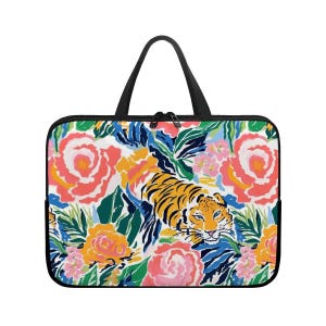 May include: A laptop sleeve featuring a vibrant floral and tiger print. The design includes a tiger amidst colorful flowers in shades of pink, orange, yellow, and green. It has a black handle and zipper.