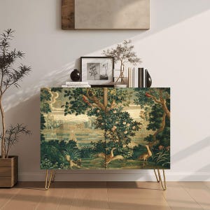 May include: A cabinet with a detailed tapestry design featuring a landscape scene with trees, birds, and animals. The cabinet has gold-colored hairpin legs. The top of the cabinet has decorative items, including books and a framed picture.