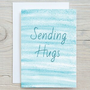 May include: A light blue card with a watercolour background and the text "Sending Hugs" in dark blue.