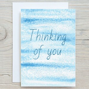 May include: A blue and white watercolour card with the text "Thinking of you" written in blue.