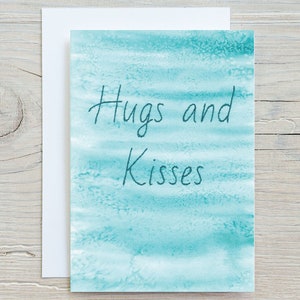 May include: A turquoise blue watercolour card with the text "Hugs and Kisses" written in black cursive.