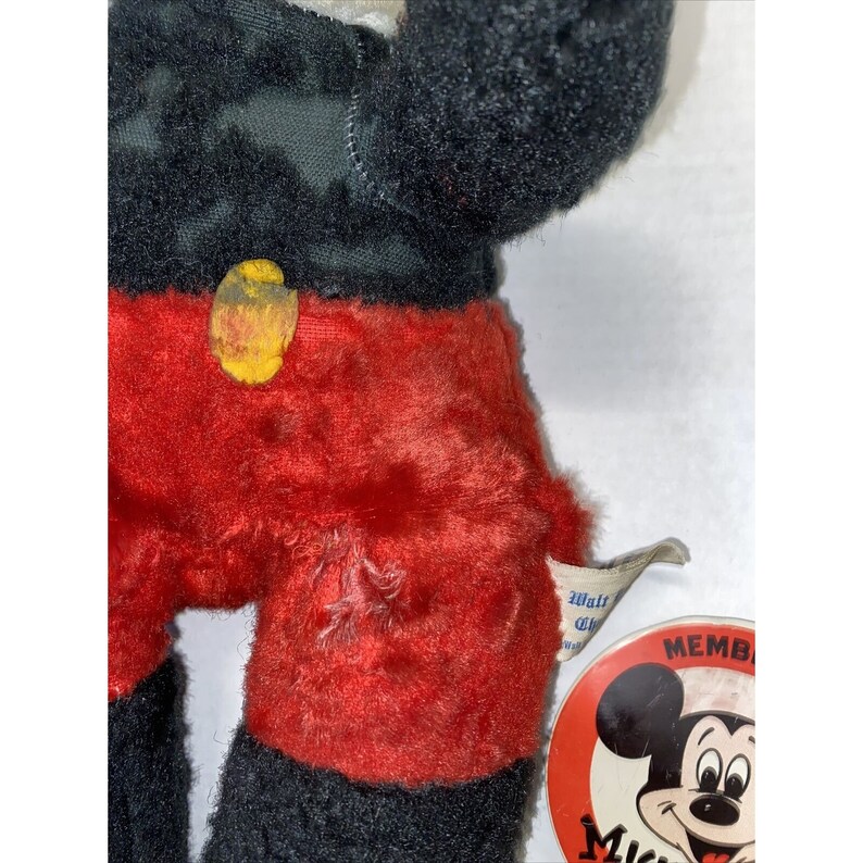 May include: Vintage plush Mickey Mouse toy with red shorts and a black and white shirt. The toy has a yellow button on its shirt and a worn tag that says "Walt Disney Productions" and "Member Mickey Mouse Club".