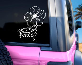 Może przedstawiać: Biała naklejka z kwiatem hibiskusa z napisem "Peace" w kursywie. Naklejka znajduje się na tylnej szybie różowego pojazdu, z plażą i palmą w tle.