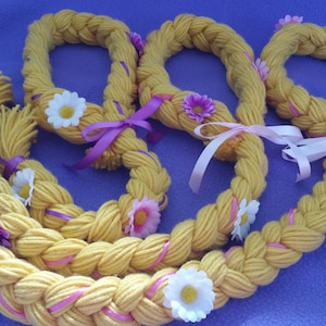 May include: A set of four yellow yarn braided hair crowns with pink and purple ribbon accents and white and purple flower embellishments.