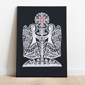 Puede incluir: Impresión de arte de papel cortado en blanco de dos ángeles que se toman de la mano con una flor en el centro. La impresión está enmarcada en un marco negro y colocada contra una pared blanca.