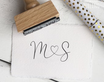 May include: A wooden stamp with a black ink pad. The stamp is used to create a design with the letters "M & S" connected by a heart.