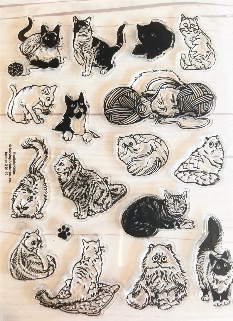 May include: Clear stamps featuring various cat illustrations in black and white. The designs include cats in different poses, with yarn balls, and a paw print. The stamps are ideal for crafting and scrapbooking projects.