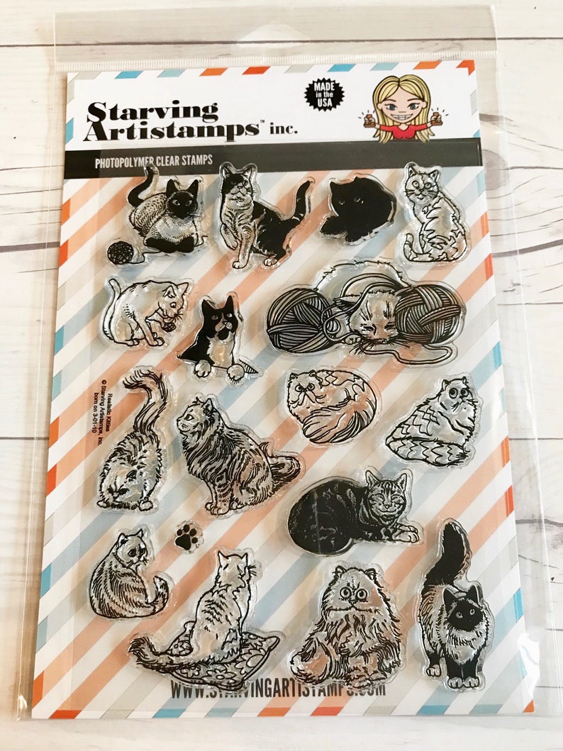 May include: Clear photopolymer stamps featuring various cat illustrations. The stamp set includes images of cats in different poses, with yarn balls, and paw prints. The packaging includes the text "Starving Artistamps inc." and "Made in the USA."