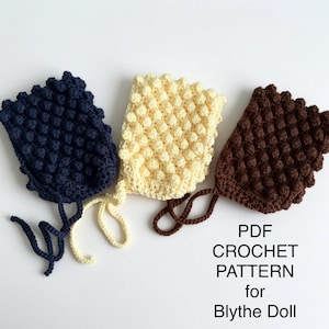 Pode incluir: Três gorros de crochê nas cores azul-marinho, creme e marrom, cada um com um padrão texturizado de pontos pipoca e tiras finas para o queixo. O texto PDF CROCHET PATTERN for Blythe Doll está impresso em preto no canto inferior direito.