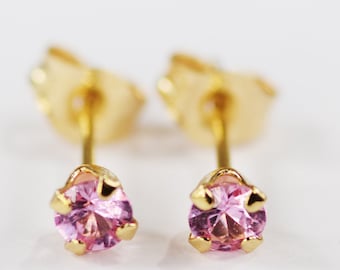 May include: A pair of stud earrings featuring a round, light pink gemstone set in a gold-colored metal. The earrings have a classic design with a post and butterfly backing. The gemstones are the focal point, catching the light.