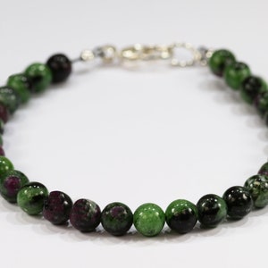 May include: A beaded bracelet featuring round, polished zoisite stones in shades of green and burgundy. The bracelet is strung on a durable cord and secured with a silver-colored clasp. The beads are approximately 0.3 inches in diameter.