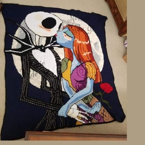 May include: A crocheted blanket featuring a scene of Jack Skellington and Sally from the Nightmare Before Christmas film. The characters are depicted kissing in front of a full moon. The blanket is made with a variety of colours, including black, white, red, and green.