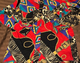 Puede incluir: Una camisa de manga larga con cuello de estilo western, que presenta un patrón geométrico en rojo, azul, negro y dorado. El diseño incluye cadenas y cinturones repetidos.