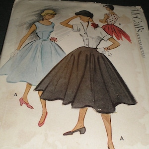 May include: Vintage McCall's sewing pattern featuring two women's dresses. The dress on the left is light blue and the dress on the right is black. The pattern is labeled "McCall's Printed Pattern".