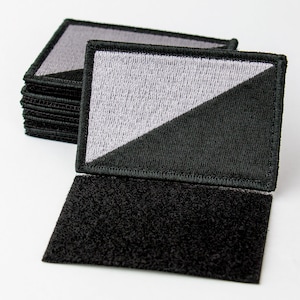 May include: A stack of black and gray embroidered patches with a diagonal line dividing the colors. The patches have a hook and loop backing.