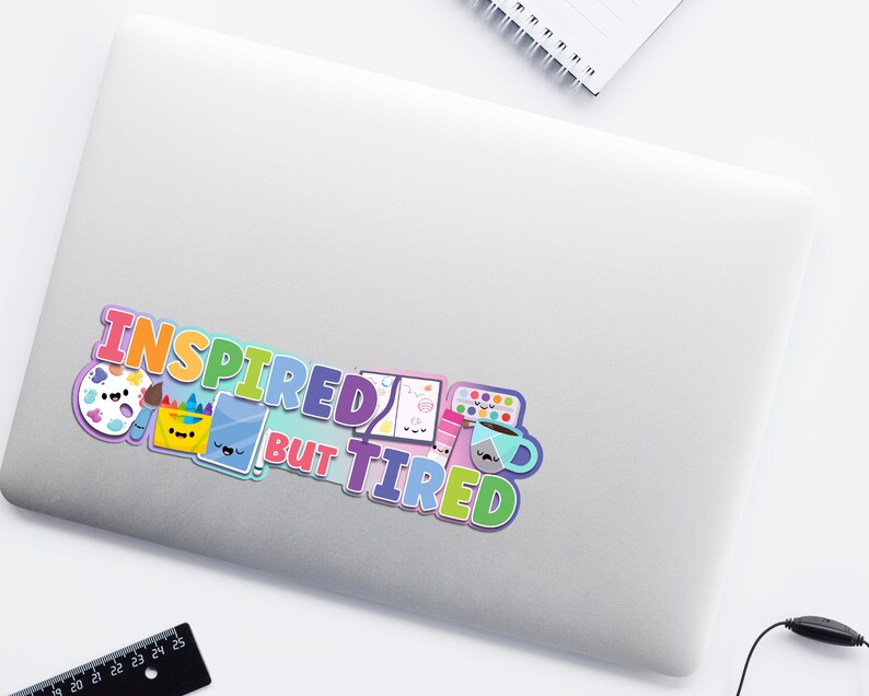 May include: A colorful sticker with the text "Inspired but Tired" and cartoon images of art supplies, including a paintbrush, paint palette, paint bucket, and a coffee mug.