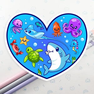 May include: A heart-shaped sticker with cartoon sea creatures. The design includes a shark, octopus, seahorse, stingray, turtle, crab, starfish, squid, and jellyfish, all in bright colours against a blue background.