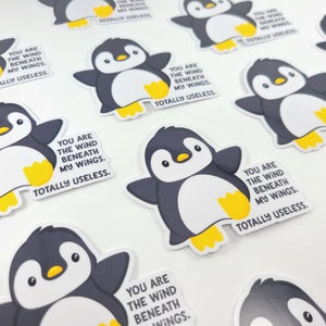 以下が含まれることがあります： 「You are the wind beneath my wings. Totally useless.」というテキストが書かれたペンギンのステッカー10枚セット。ペンギンは黒と白で、黄色いアクセントが付けられています。