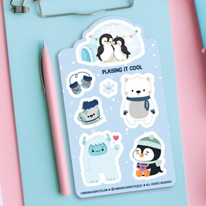 Puede incluir: Un conjunto de seis pegatinas de tem&aacute;tica invernal con un oso polar, ping&uuml;inos, un yeti y accesorios de invierno. Las pegatinas est&aacute;n sobre un fondo azul con el texto "Playing it Cool".