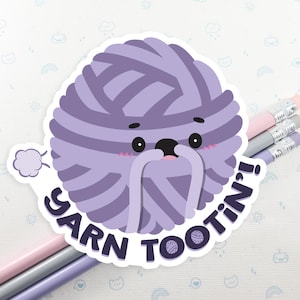 May include: Purple ball of yarn with a cute face and the text "Yarn Tootin'!".