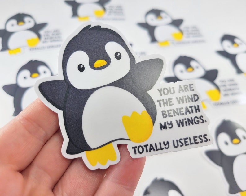 以下が含まれることがあります： 「You are the wind beneath my wings. Totally useless.」というテキストが書かれた、漫画のペンギンが描かれたステッカーです