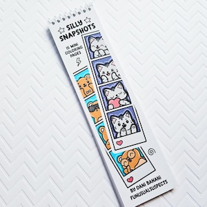 May include: A spiral-bound coloring book titled "Silly Snapshots" featuring 15 mini coloring pages. The cover displays cartoon cats and bears in polaroid-style frames. The book is white with black and blue accents, and the artist's name is visible.
