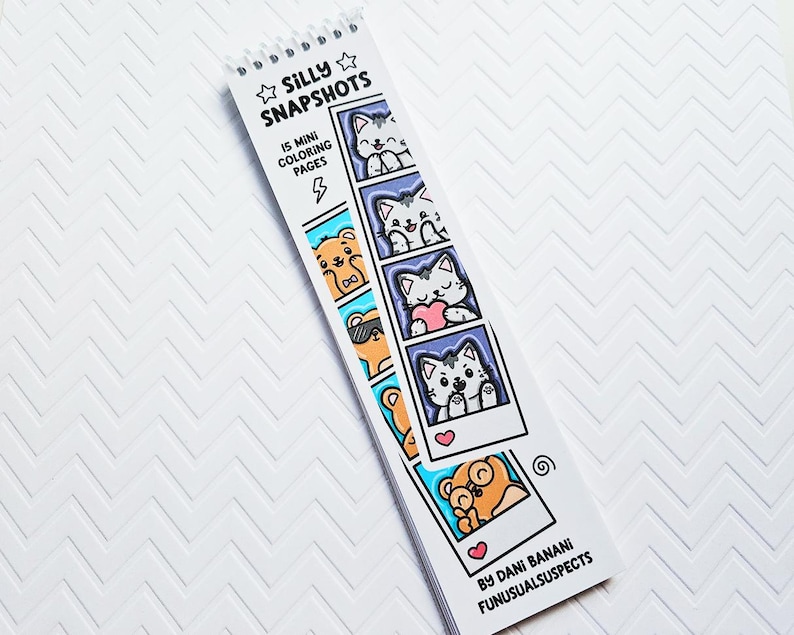 May include: A spiral-bound coloring book titled "Silly Snapshots" featuring 15 mini coloring pages. The cover displays cartoon cats and bears in polaroid-style frames. The book is white with black and blue accents, and the artist's name is visible.