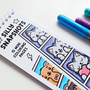 May include: A spiral-bound coloring book titled "Silly Snapshots" with 15 mini coloring pages. The pages feature cartoon cats and bears. Blue, purple, teal, and red markers are placed next to the coloring book.