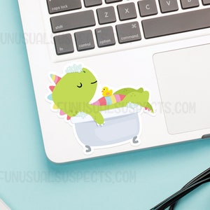 May include: A green dinosaur with a pink and blue striped tail is taking a bath in a white bathtub with a yellow rubber ducky. The dinosaur has a pink and white flower on its head and is surrounded by white bubbles.
