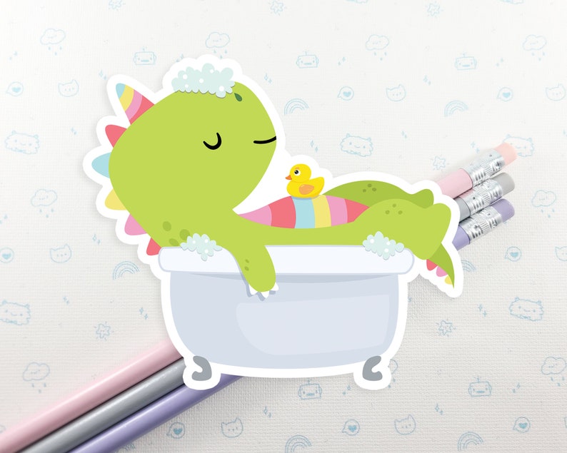May include: A green dinosaur with a rainbow tail is taking a bath in a white bathtub. The dinosaur has a yellow rubber ducky in the tub with it. The dinosaur is smiling and has its eyes closed.