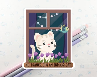 May include: A white cat with brown stripes looks out of a window with a string of lights. The cat is sitting on a windowsill with purple flowers. The text "NO THANKS, I'M AN INDOOR CAT." is below the window.