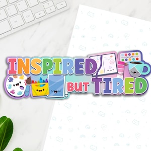 May include: A colorful graphic design with the text "Inspired But Tired" and cartoon images of art supplies, including a paint palette, crayons, a sketchbook, and a coffee cup.