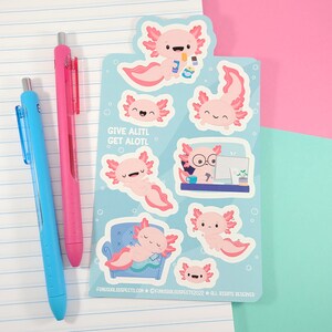 K&ouml;nnte beinhalten: Eine Bogen mit Aufklebern, die verschiedene Illustrationen von rosa Axolotl in verschiedenen Posen zeigen. Die Aufkleber befinden sich auf einem hellblauen Hintergrund mit wei&szlig;en Blasen. Der Text "GIVE ALITL GET ALOTL" ist auf dem Bogen gedruckt.
