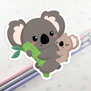 May include: A gray koala holding a green bamboo stick with a smaller gray koala clinging to its back. Both koalas have black eyes and pink noses.