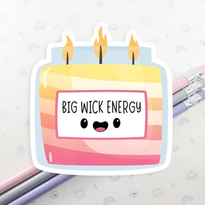 Może przedstawiać: Naklejka z kresk&oacute;wkową świecą z uśmiechającą się twarzą i tekstem "BIG WICK ENERGY". Świeca jest ż&oacute;łta, pomarańczowa i r&oacute;żowa z niebieskim wieczkiem.