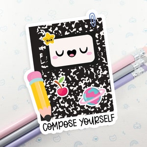 May include: A white sticker with a black and white notebook design. The notebook has a cute cartoon face with a star, a cherry, and a planet on it. The sticker says "Compose Yourself".
