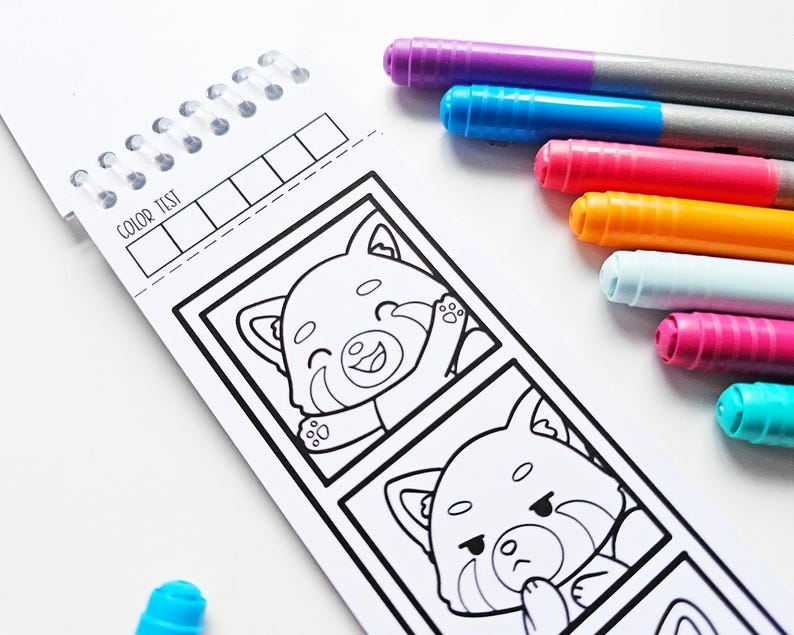 May include: A spiral-bound coloring book with red panda illustrations and the text "COLOR TEST." Several colorful markers in purple, blue, pink, orange, white, and teal are arranged next to the book, ready for use.