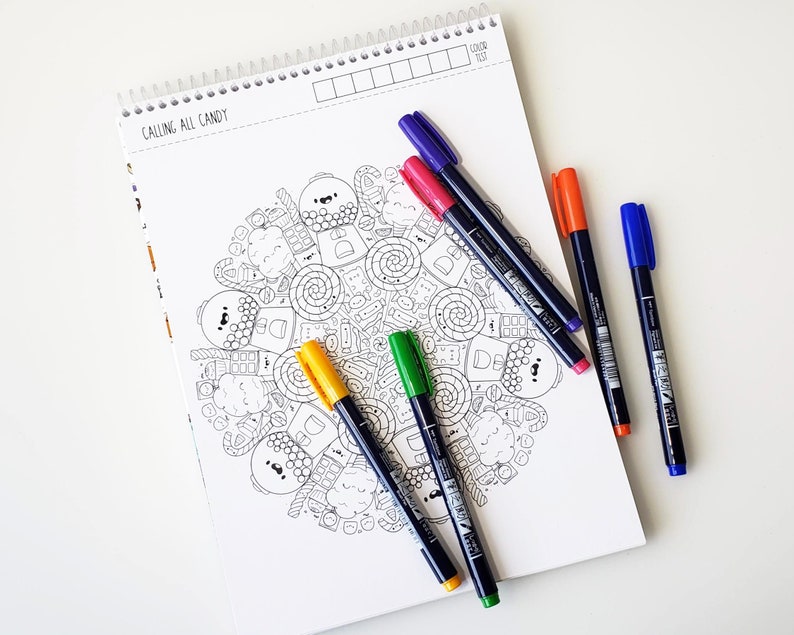 May include: A coloring book page with a mandala design featuring candy and sweets. The page is titled "Calling All Candy". Five different colored markers are laid out on the page.