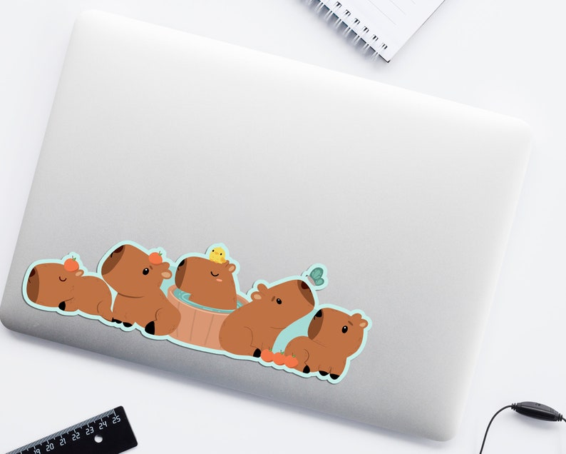 May include: A sticker featuring a group of five brown capybaras. One capybara is in a blue tub with a yellow bird on top. Another capybara has a butterfly above its head. The capybaras are all smiling and have orange accents on their ears.