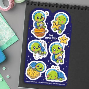 May include: A set of six stickers featuring cute cartoon turtles in space. The turtles are wearing astronaut helmets and are holding stars, planets, and other space-themed objects. The stickers are printed on high-quality vinyl and are perfect for decorating laptops, water bottles, notebooks, and more. The stickers say "One Small Step".