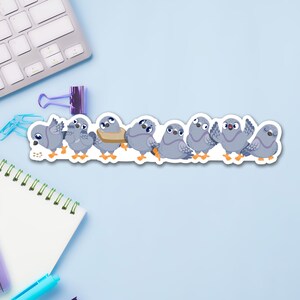 May include: A sticker featuring a line of cartoon pigeons in various poses. The pigeons are primarily gray with orange feet and beaks. One pigeon wears a tan scarf. The sticker is on a light blue surface with office supplies.
