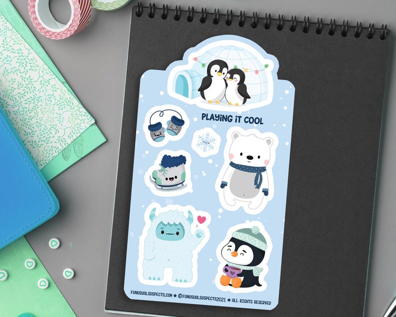 Puede incluir: Un conjunto de seis pegatinas de tem&aacute;tica invernal con un oso polar, ping&uuml;inos, un yeti, guantes y patines. Las pegatinas est&aacute;n sobre un fondo azul con el texto "Playing it Cool".