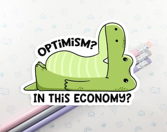 May include: A green cartoon alligator sticker with the text "OPTIMISM? IN THIS ECONOMY?" The alligator is lying down with its mouth open. Pencils are in the background.