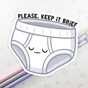 May include: A white sticker with a cartoon pair of briefs with a smiling face. The text "PLEASE, KEEP IT BRIEF" is printed above the underwear. Three pencils with pink, grey, and purple erasers are visible.