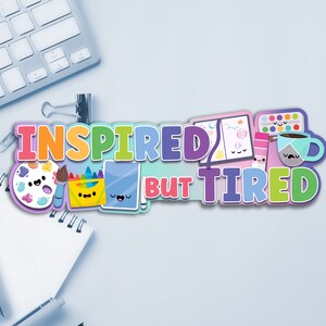 May include: A colorful graphic design with the text "Inspired but Tired" featuring a paint palette, paintbrushes, crayons, a notebook, a coffee cup, and a paint can with cute cartoon faces.