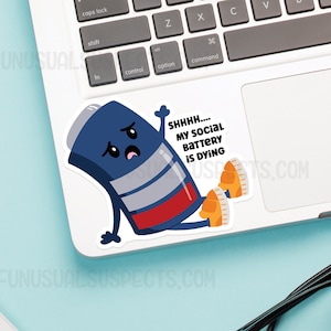 K&ouml;nnte beinhalten: Ein blauer und roter Batterie-Charakter mit einem traurigen Gesicht und dem Text "SHHHH.... MY SOCIAL BATTERY IS DYING" auf einem wei&szlig;en Laptop.